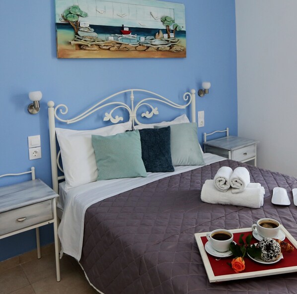 A neatly made bed with a quilted cover, two bedside tables, a wall-mounted painting, and a tray with breakfast items. - kastro hotel (Skiathos)