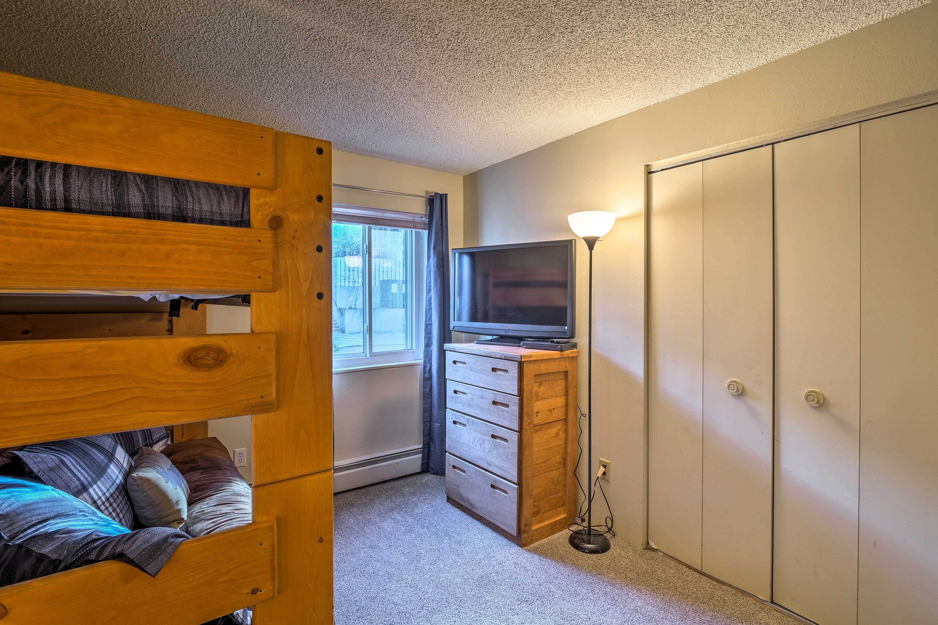 Ein Stockbett mit Kissen, ein Schminktisch, ein Fernseher und ein Kleiderschrank in einem Zimmer mit Fenster und Teppichboden.