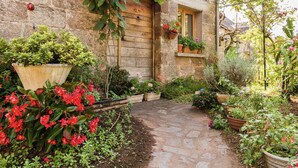 A stone building with a wooden door and window, surrounded by a garden with various potted plants and flowers.
