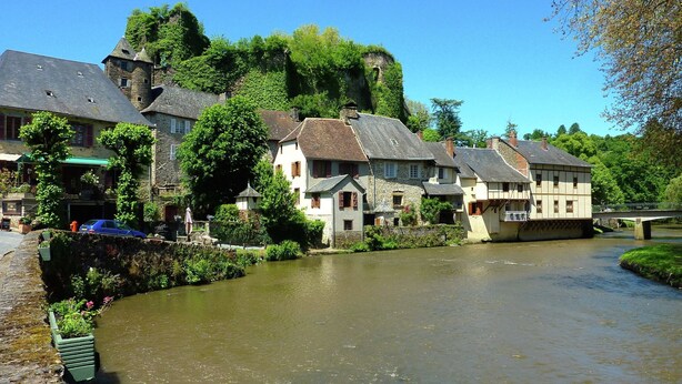 A riverside town with stone buildings, a bridge, and lush greenery.