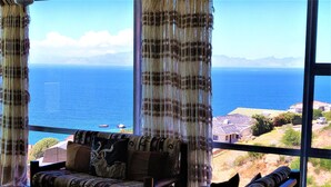 A room with a large window overlooking the sea, a sofa, and a coffee table.