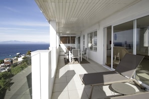 Enjoy breathtaking views of the sea and distant mountains from this balcony, featuring a table and two chairs.