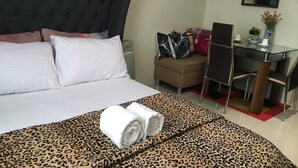 Une chambre d’hôtel avec un grand lit, un bureau et une chaise. On y trouve une petite table sur laquelle est posé un vase de fleurs.