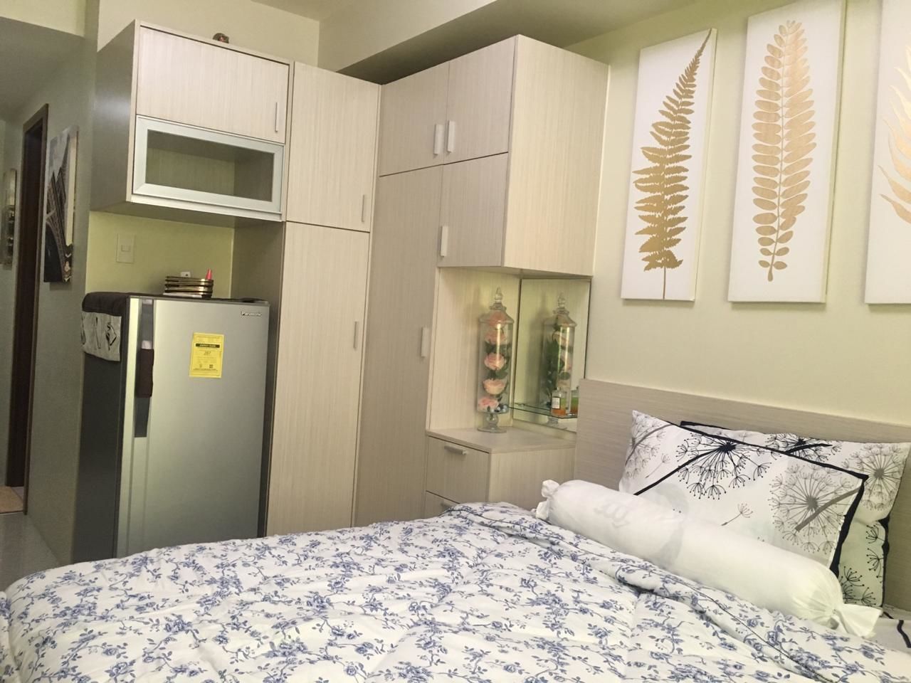 Een slaapkamer met een bed, een koelkast, een spiegel en een klein kastje.