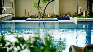 Une piscine avec une petite île au centre, entourée de plantes et de quelques sculptures.