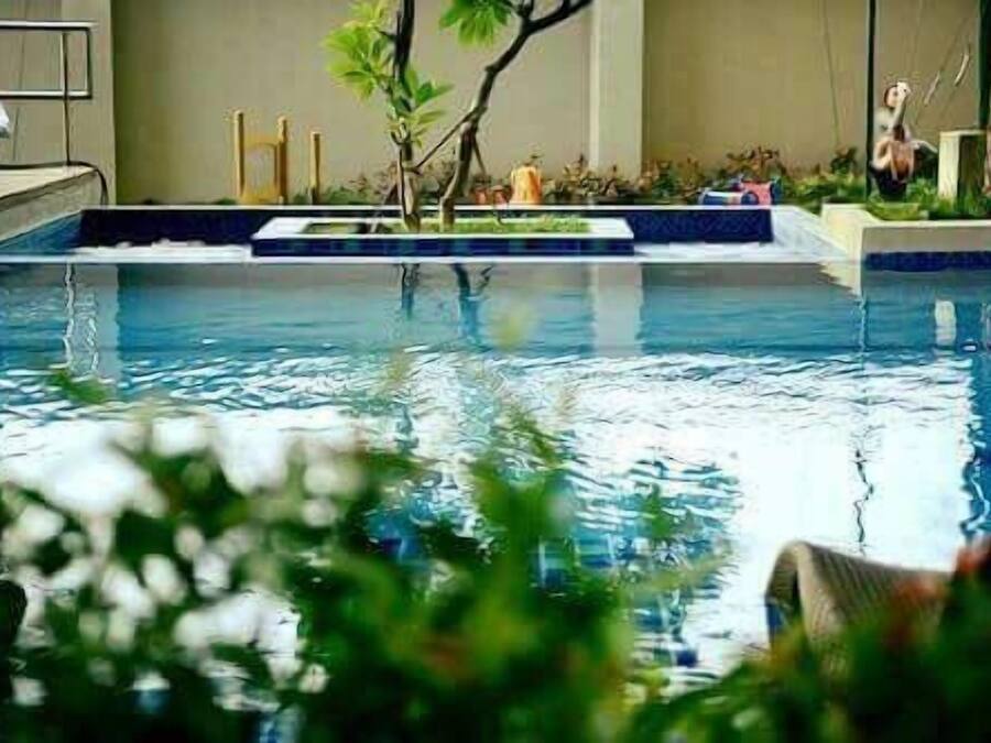 Une piscine avec une petite île au centre, entourée de plantes et de quelques sculptures.
