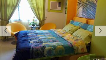 A bedroom with a bed, two chairs, a small table, and a window with curtains.