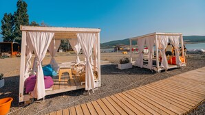 Deux tentes blanches avec des coussins et une table, installées sur une terrasse en bois près d’une plage.