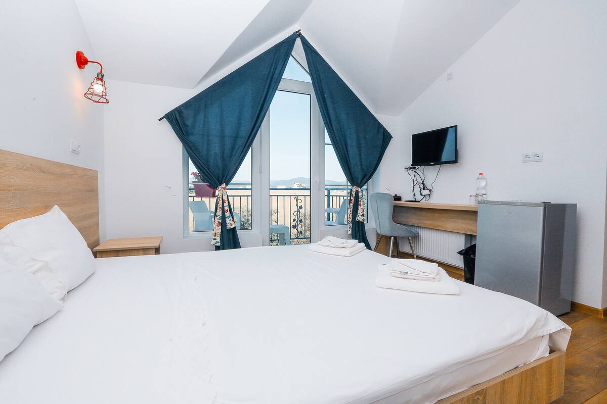 Una habitación de hotel con una cama grande, un escritorio, un televisor y un balcón con cortinas.