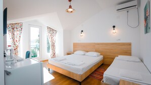 Une chambre d’hôtel moderne avec un lit en bois, un petit bureau et une fenêtre agrémentée de rideaux à motifs floraux.