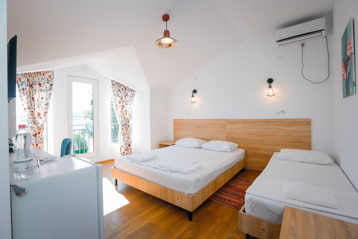 Una habitación de hotel moderna con una cama de madera, un escritorio pequeño y una ventana con cortinas florales.