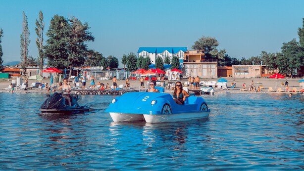 Un plan d’eau avec des bateaux et une plage aménagée avec des parasols et des personnes.
