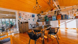 Un vaste espace de salle à manger avec une table et des chaises en bois, un coin cuisine équipé de divers appareils et agrémenté de décorations, et de grandes fenêtres laissant entrer la lumière naturelle.