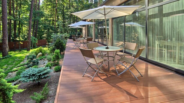 Une terrasse extérieure dotée d’un plancher en bois, de chaises en osier et de parasols, entourée d’une zone boisée.