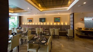 A restaurant with booths and tables, a TV mounted on the wall, and a ceiling with recessed lighting. - St Parklane Airport Hotel Chennai (Chennai)