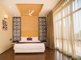 Um quarto espaçoso com uma cama grande, um ventilador de teto e vista para o exterior através de cortinas finas.