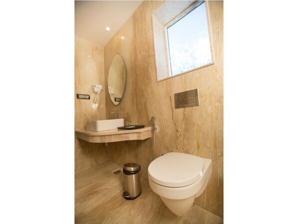 Un baño con pared de mármol, un lavabo, un inodoro, un espejo y una ventana.
