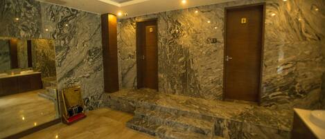 Un baño con piso de mármol, un espejo grande, un lavamanos y tres puertas de madera.