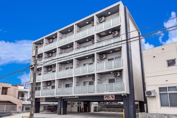 Um edifício com vários andares, entrada central, varandas e aparelhos de ar condicionado.