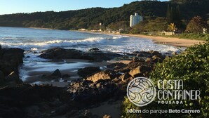 A coastal view with rocky shoreline, beach, and a hill with buildings in the background.