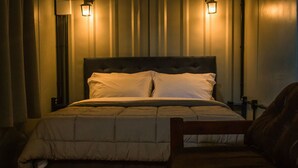 A neatly made bed with a dark headboard and white bedding, flanked by two wall-mounted lamps.