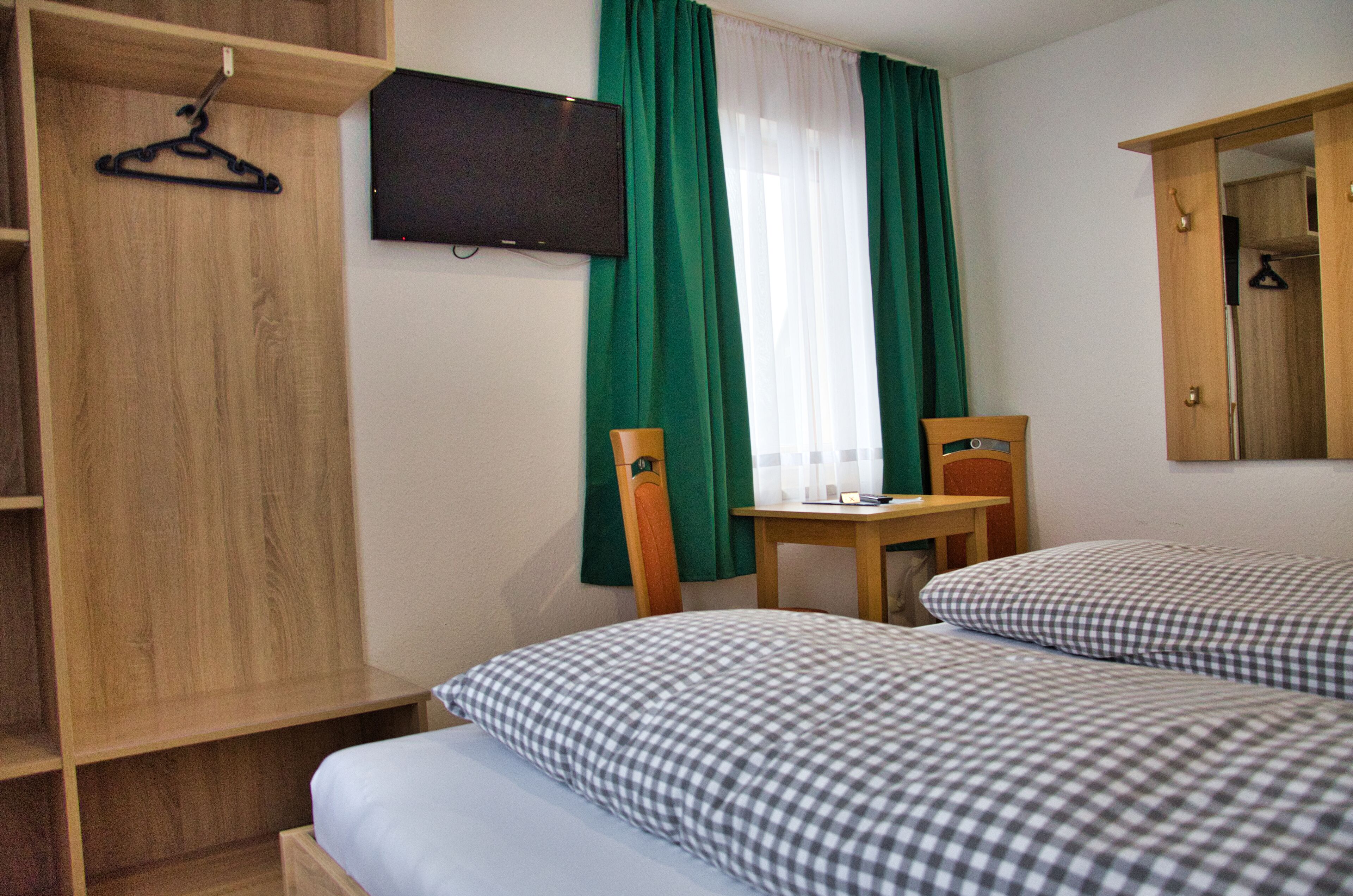 Habitación de hotel con dos camas, un armario de madera, un escritorio, una silla, un televisor y una ventana con cortinas verdes.