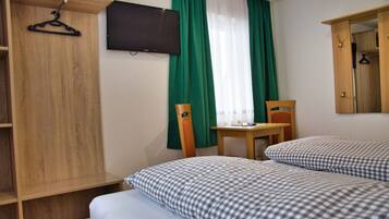 Habitación de hotel con dos camas, un armario de madera, un escritorio, una silla, un televisor y una ventana con cortinas verdes.