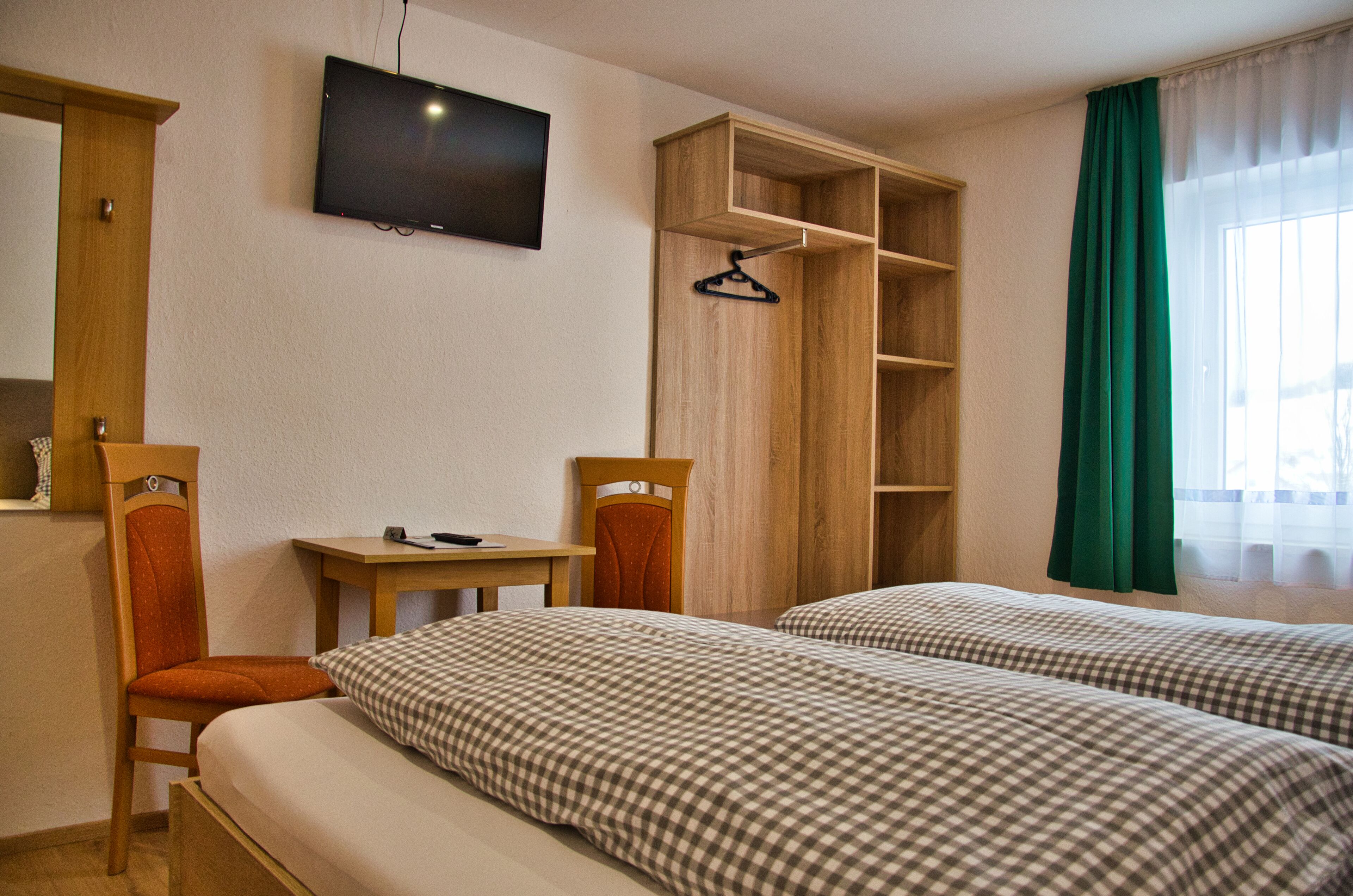 A hotel room with two beds, a TV, a wooden wardrobe, and a desk.