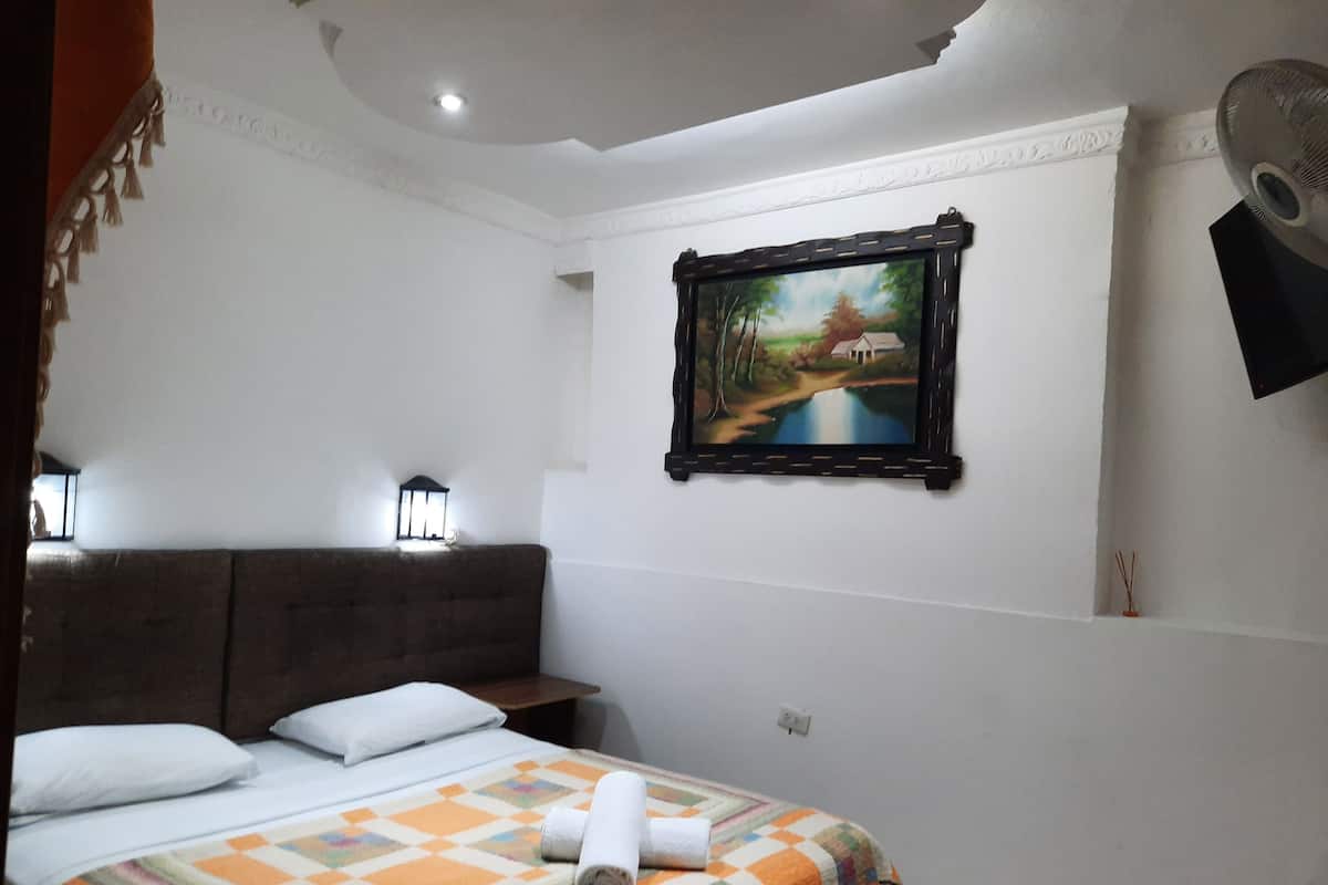 Una habitación de hotel con cama, un cuadro en la pared y una mesita de noche con lámpara.