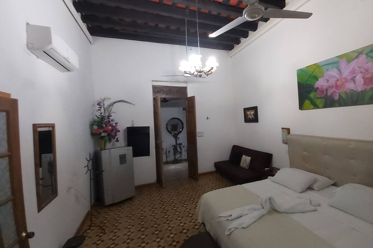 Un dormitorio con cama, ventilador de techo, un cuadro de flores y espejo.