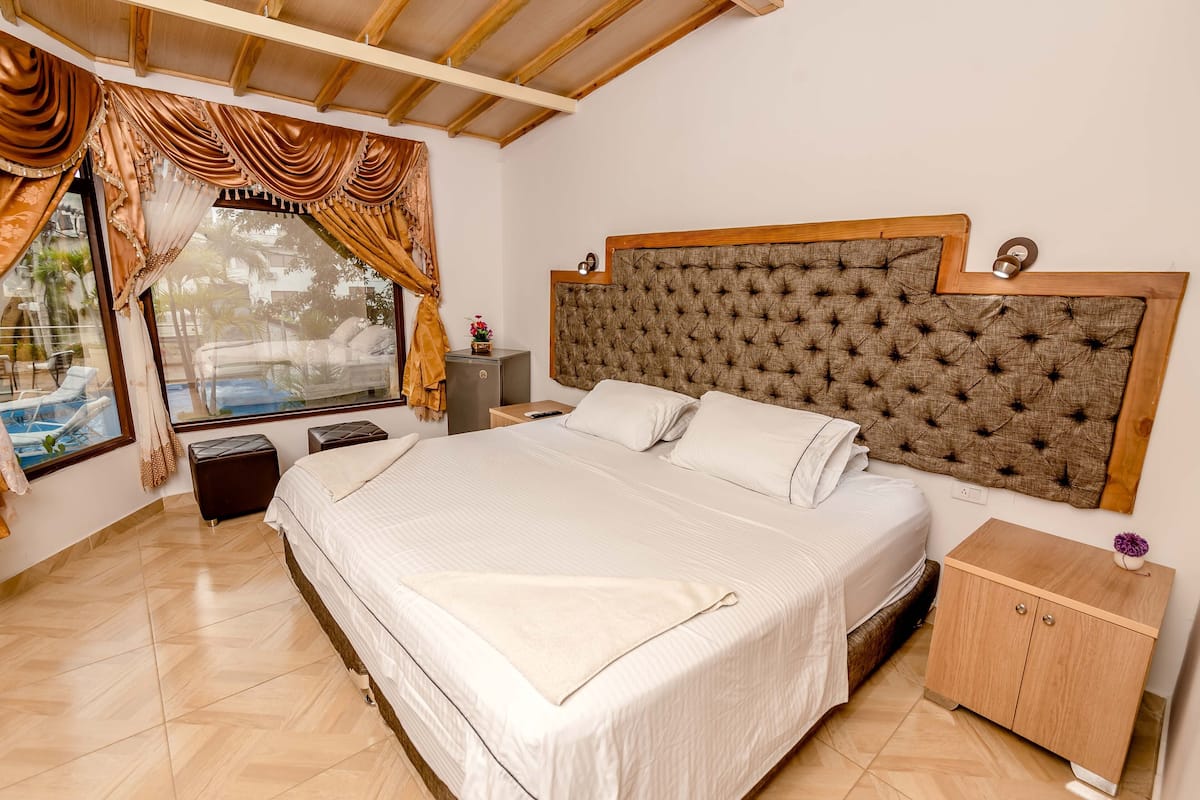 Un dormitorio con una cama grande, un cabecero de madera, una mesita de noche, un armario de madera y una ventana con cortinas.