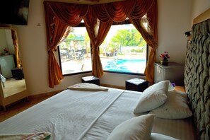 A hotel room with a bed, a window with curtains, a small table, a mirror, and a TV mounted on the wall.
