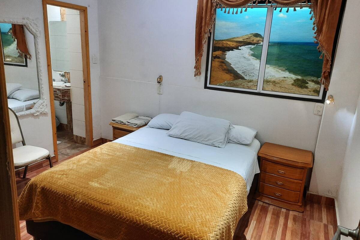 Un dormitorio con cama, mesita de noche, cómoda, ventana con vista al mar y espejo.
