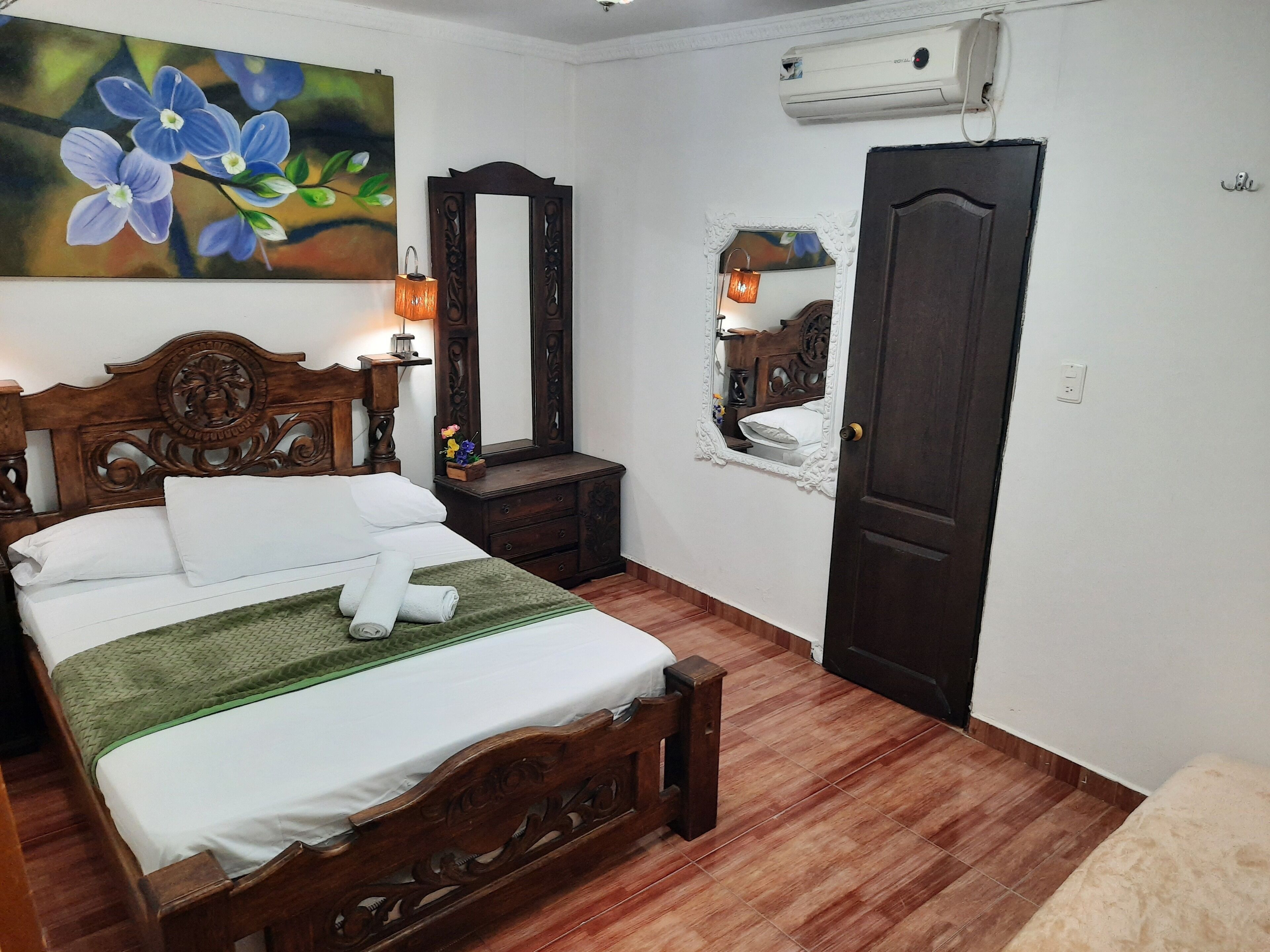Un dormitorio con una cama de madera, una mesita de noche, un espejo y un aire acondicionado.