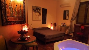 Una habitación con una cama grande, una zona de estar con una mesa y sillas, un jacuzzi y obras de arte en las paredes.