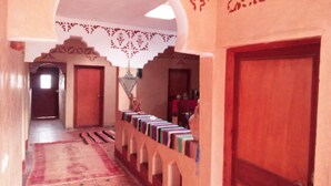 A hallway with a patterned rug, a row of bookshelves, and a wooden door. - Dar Zara (Ighrem N'Ougdal)