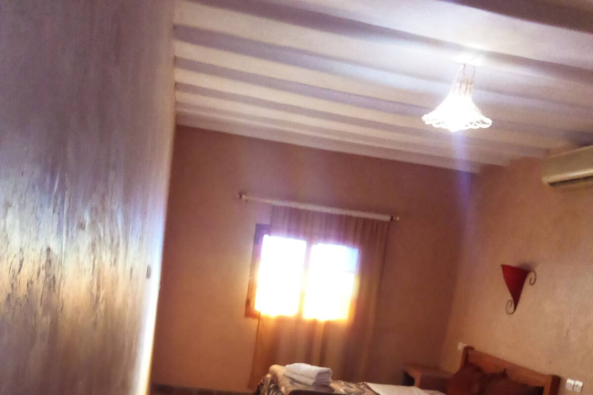 A narrow hallway leading to a bedroom with a bed, a window with curtains, and a ceiling fan.