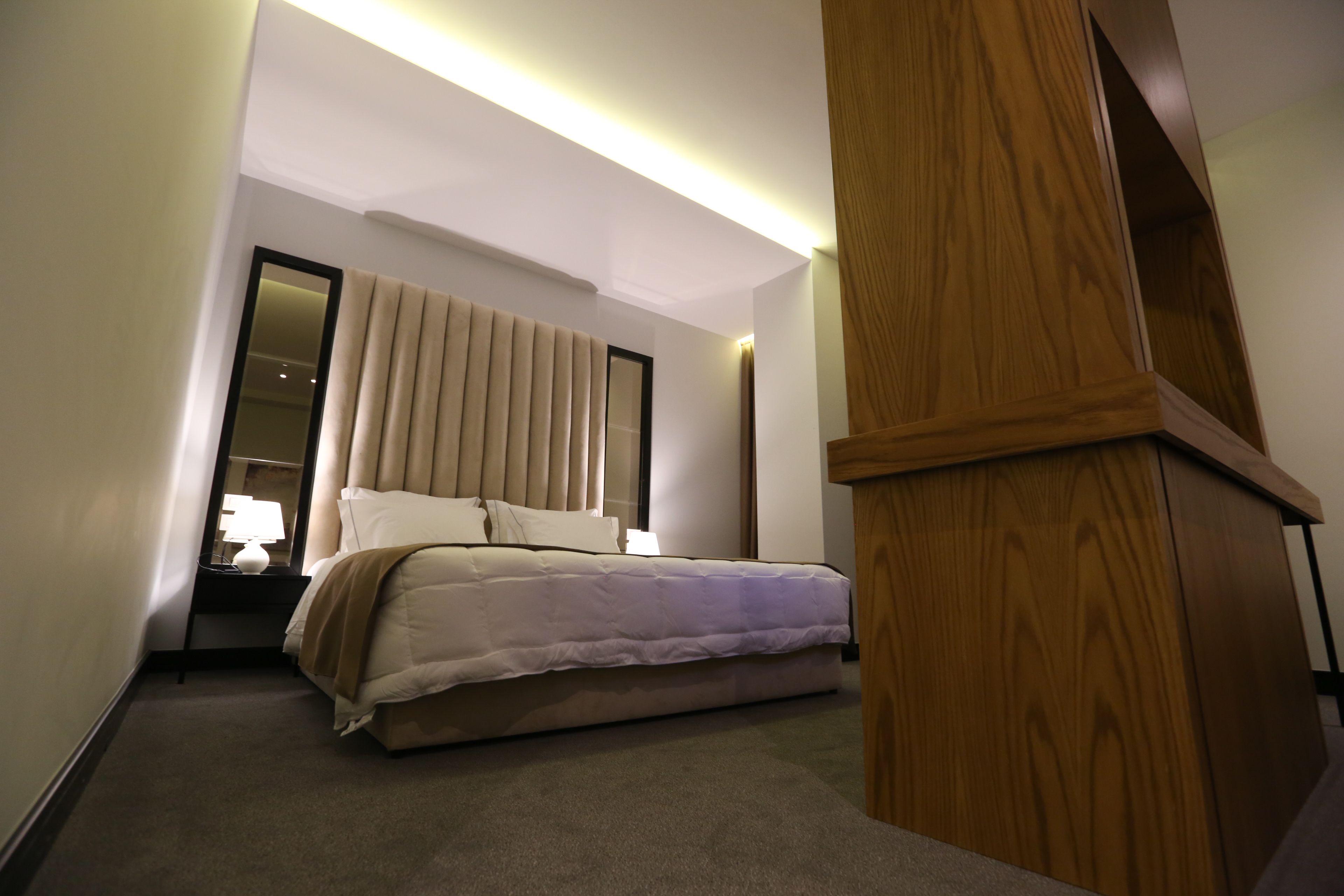 Una habitación de hotel con cama, mesita de noche, espejo y panel de madera.