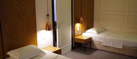 A hotel room with two beds, a wooden wardrobe, a desk, and a door.