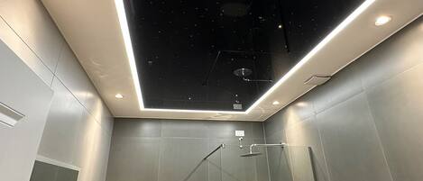 A modern bathroom with a starry ceiling design, recessed lighting, and a glass shower enclosure.