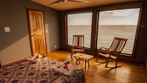 A room with a bed, two rocking chairs, a small table, and a large window overlooking the ocean. - Magnific Rock - Surf Resort & Yoga Retreat Nicaragua - Hostel (Tola)