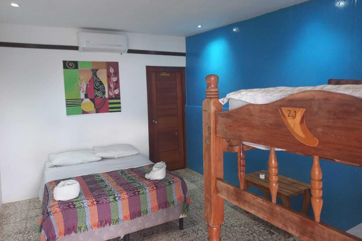 A room with a bed, a bench, a door, and a wall-mounted air conditioner.