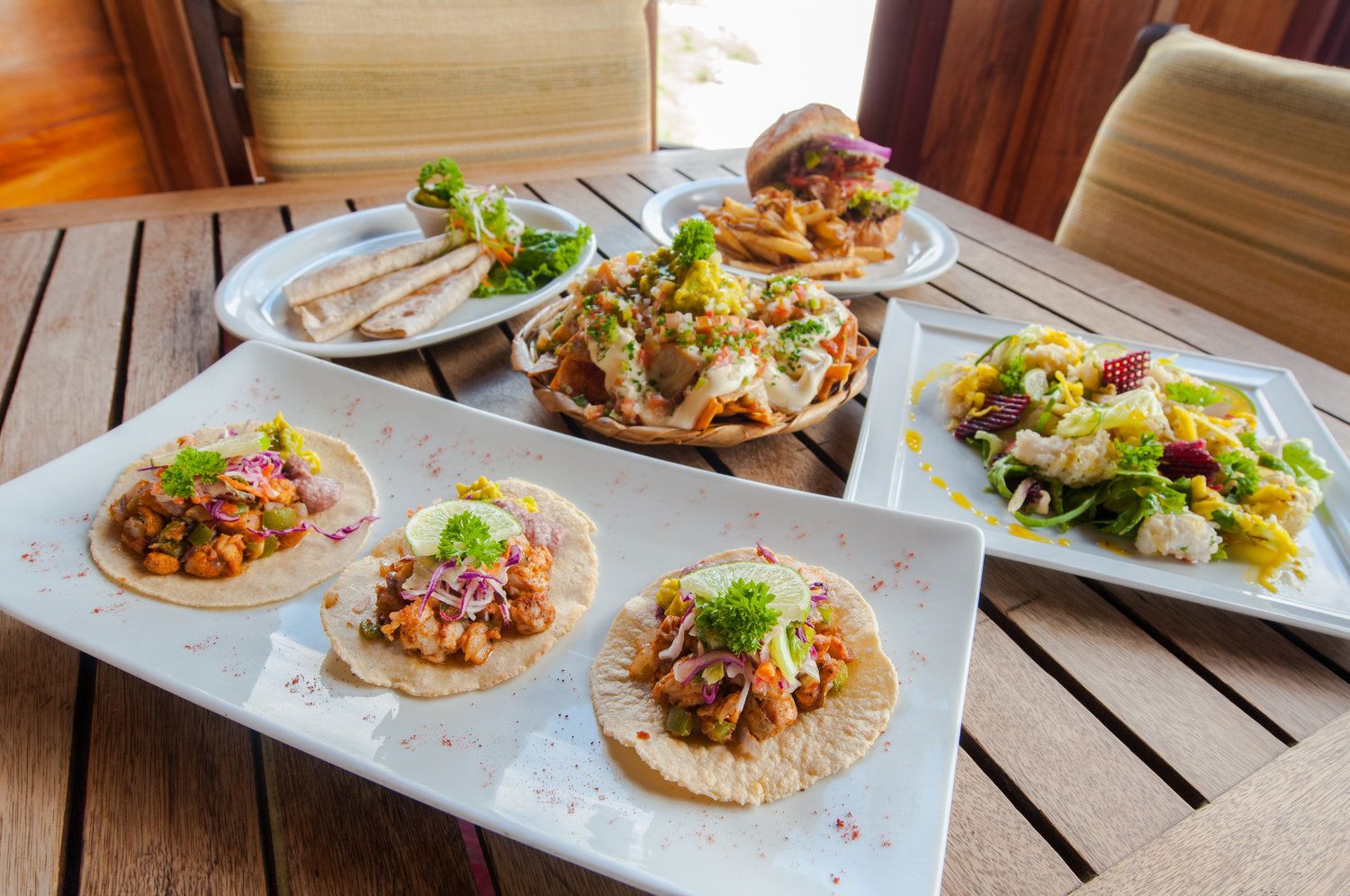 Una mesa con varios platos, incluyendo tacos, papas fritas y una ensalada.