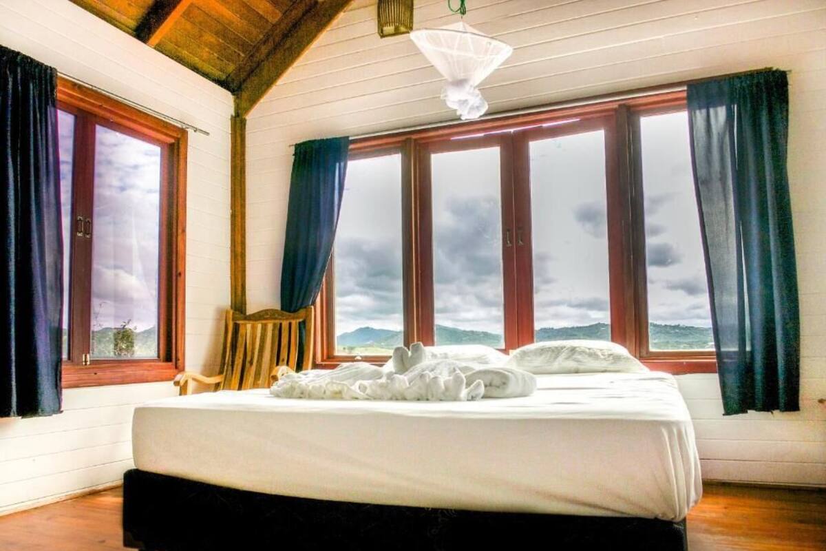 A bedroom with a bed, large windows, and a view of the outdoors.