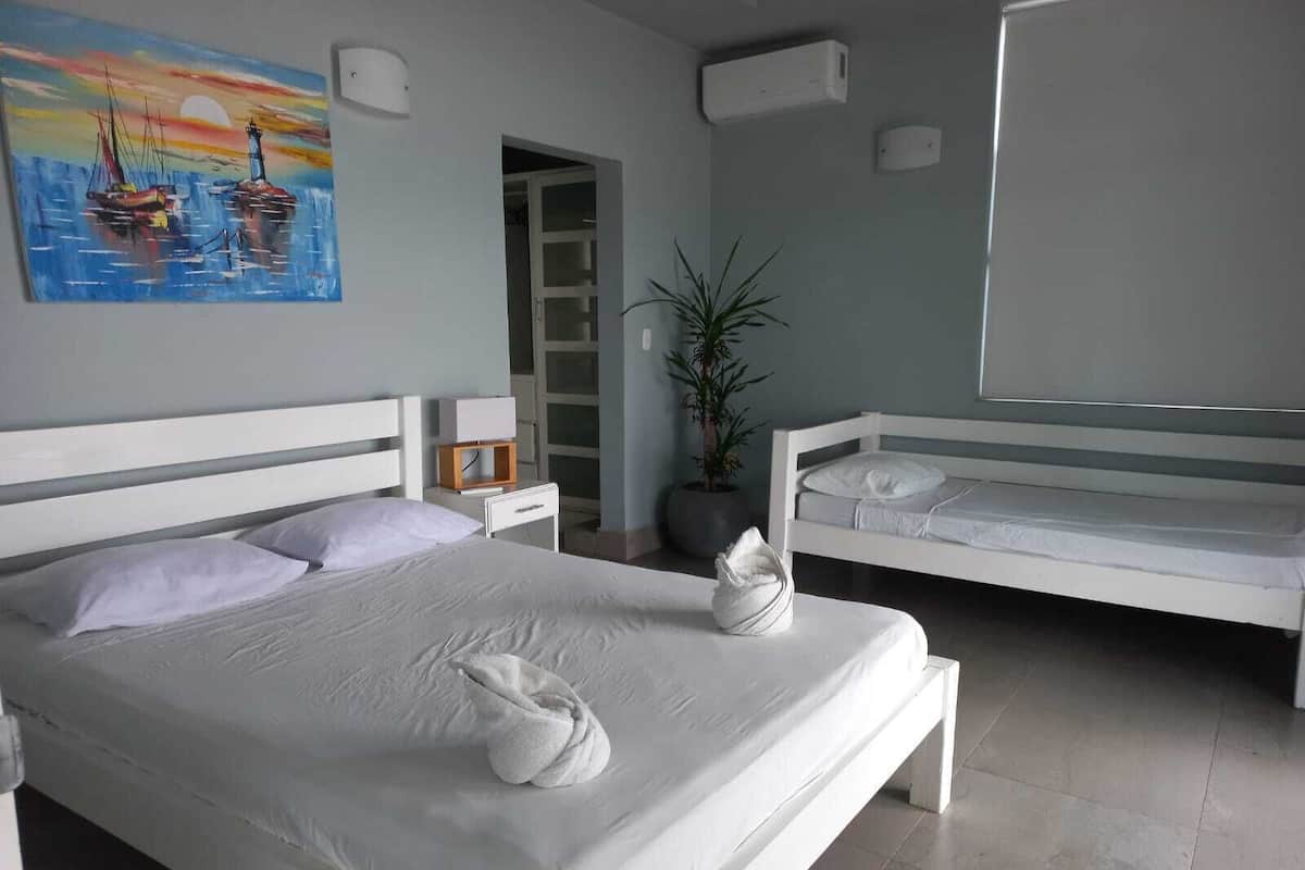 A modern hotel room with a large bed, a smaller bed, a potted plant, and a painting of boats on the wall.
