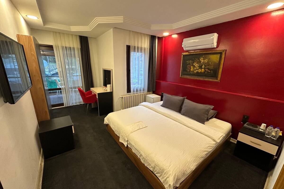 Une chambre d’hôtel avec un grand lit, un bureau, une chaise, une télévision et un mur d’accent de couleur rouge.