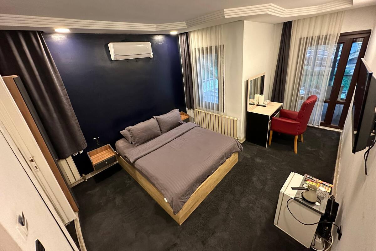 Une chambre d’hôtel avec un lit, un bureau, une chaise, une télévision et une fenêtre avec des rideaux.