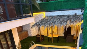 Una piscina con zona de estar cubierta por un techo de paja y vegetación circundante.