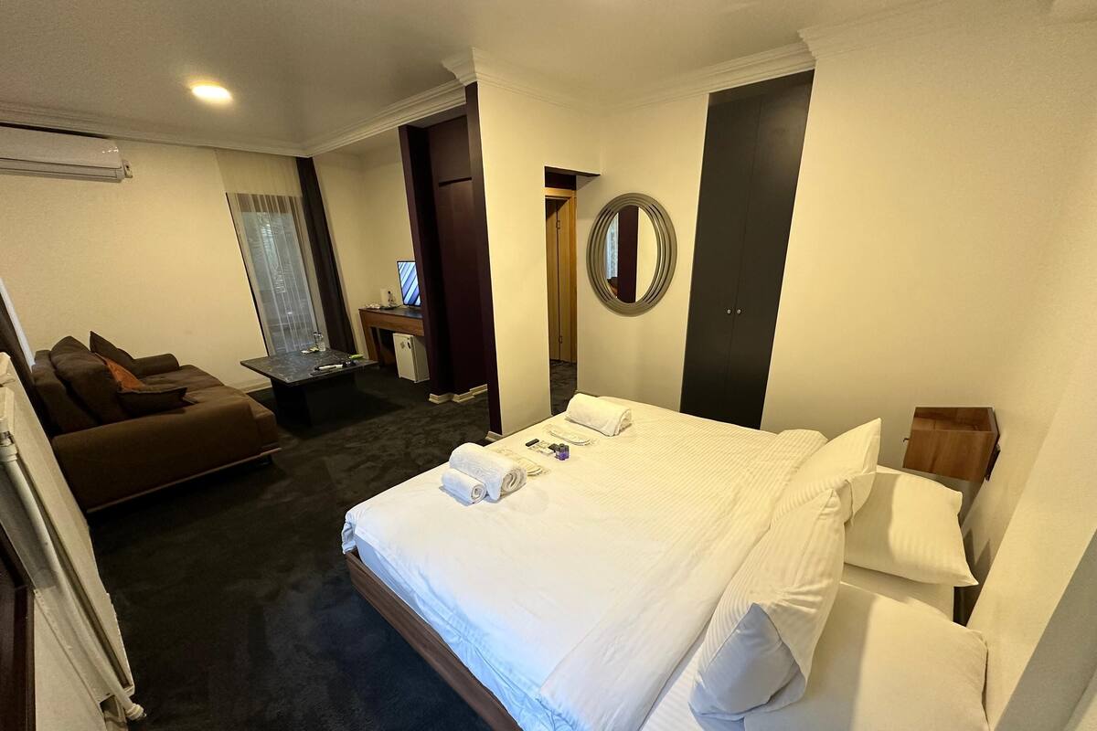 Une chambre d’hôtel avec un grand lit, un canapé, un bureau avec un ordinateur, un miroir et une petite salle de bain.