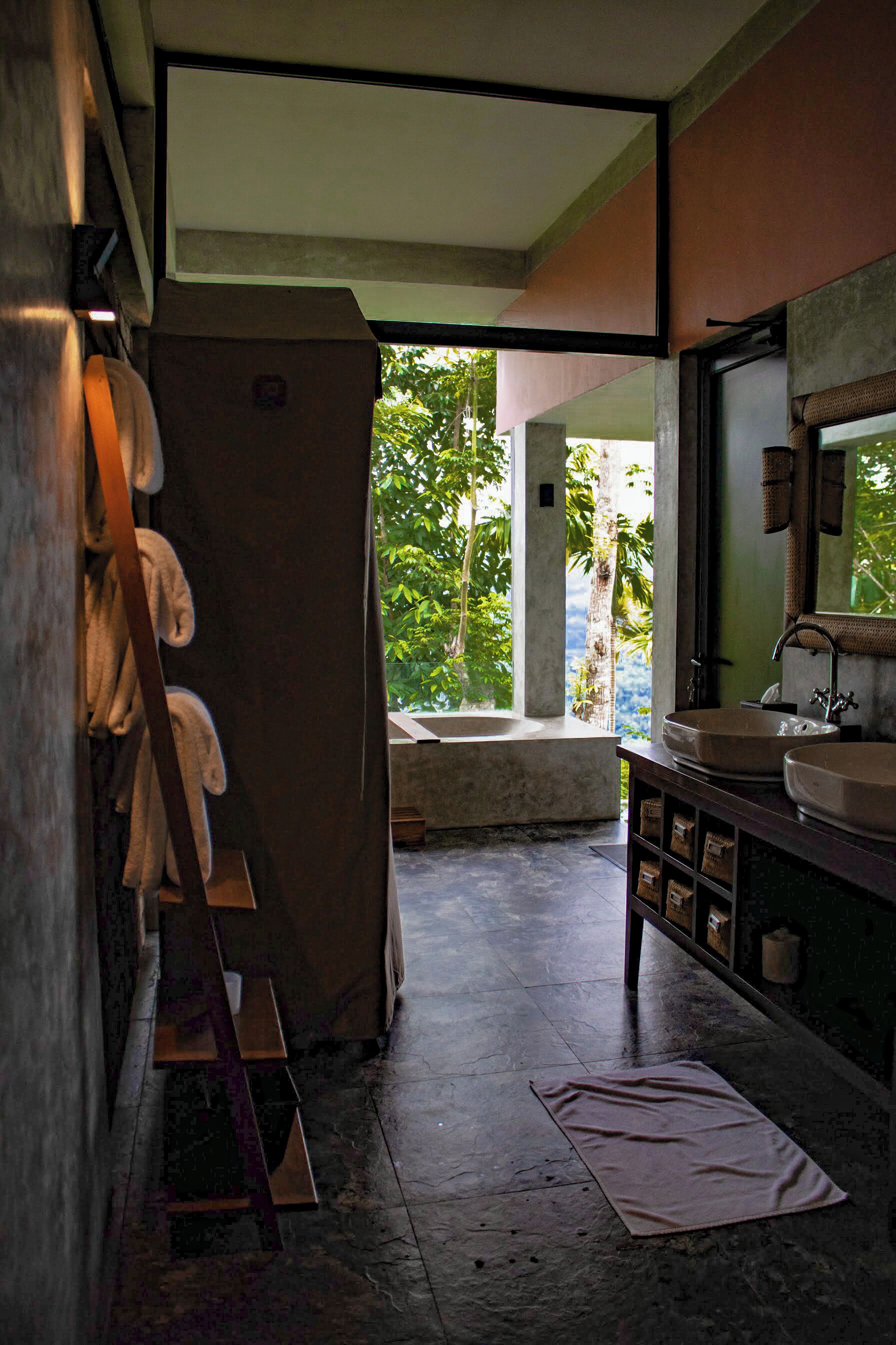 A bathroom with a large bathtub, a sink, and a mirror. There is a towel rack and a shelf with towels.